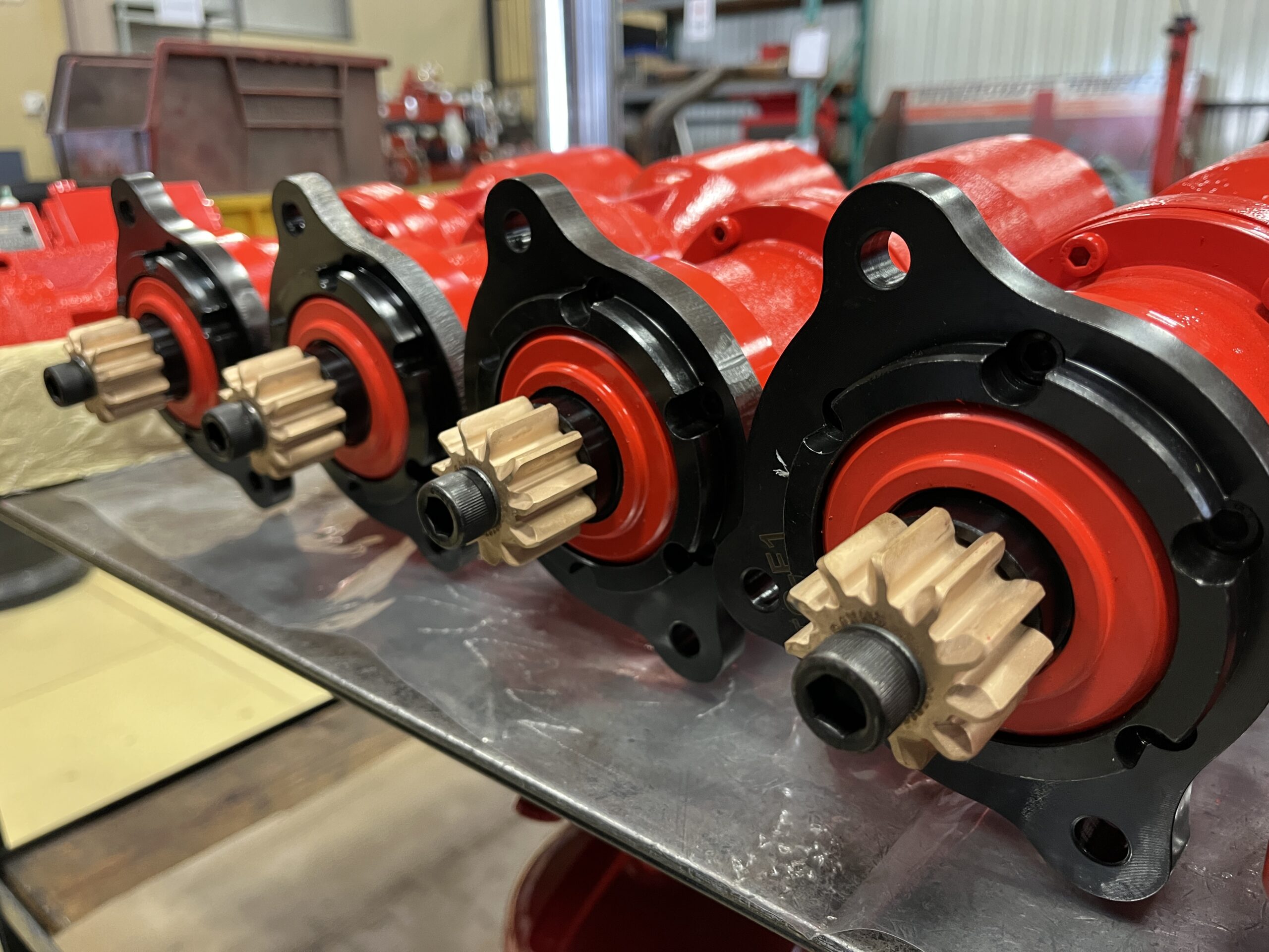 Powerstart M-series hydraulic starter motors lined up during assembly at the UK facility, showing cast iron red housings and brass pinion gears