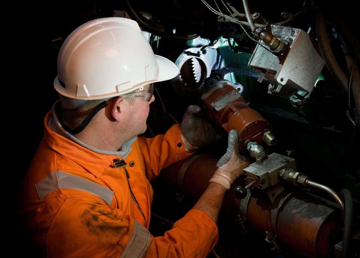 Engineer in orange PPE fitting an air starter to a diesel engine flywheel ring gear